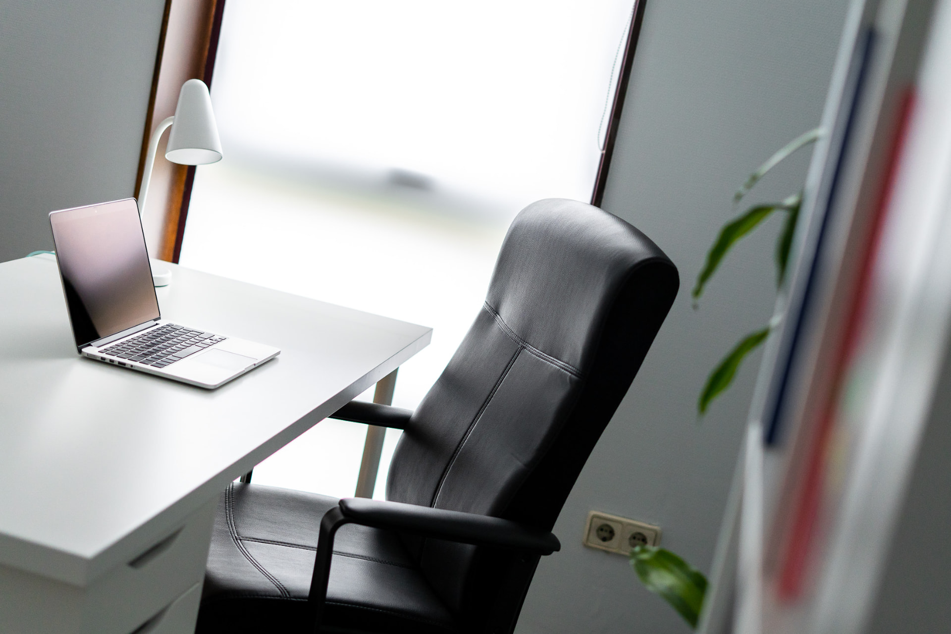 Despacho de trabajo con escritorio blanco, silla ergonómica, portátil y plantas junto a la ventana