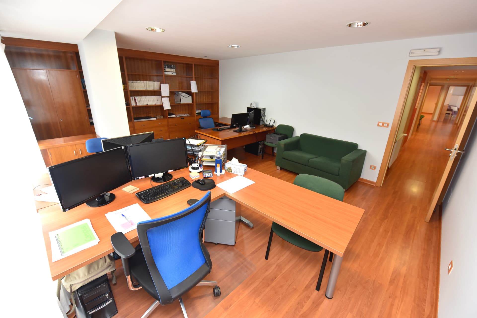 Oficina de CNG Solutio Lugo con varios escritorios, monitores, estanterías de madera y un sofá verde