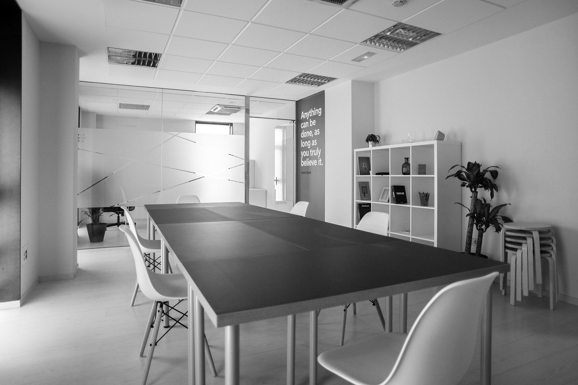 Sala compartida de A Coruña con mesa central alargada, sillas blancas y estantería al fondo.