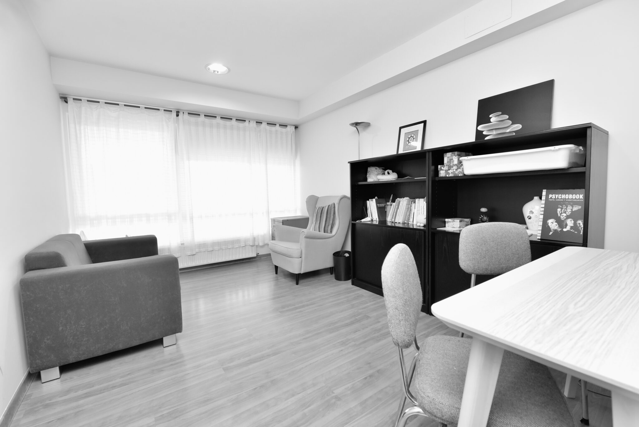 Oficina de Lugo con sofá, butaca, mesa de trabajo en primer plano y estantería baja en la pared.