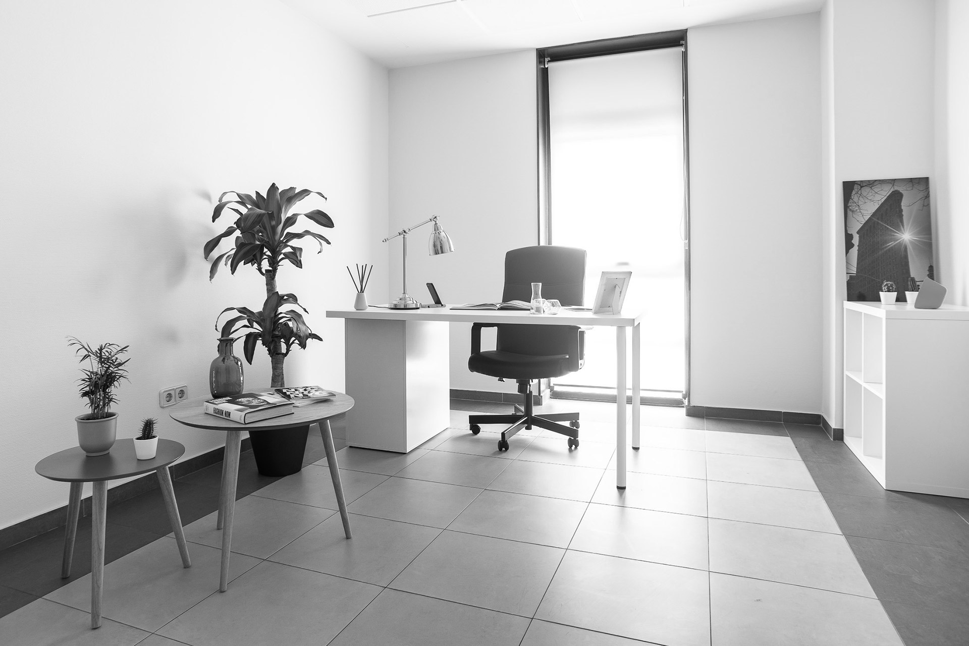 Despacho individual de A Coruña con mesa blanca, silla de oficina, plantas y ventana amplia.
