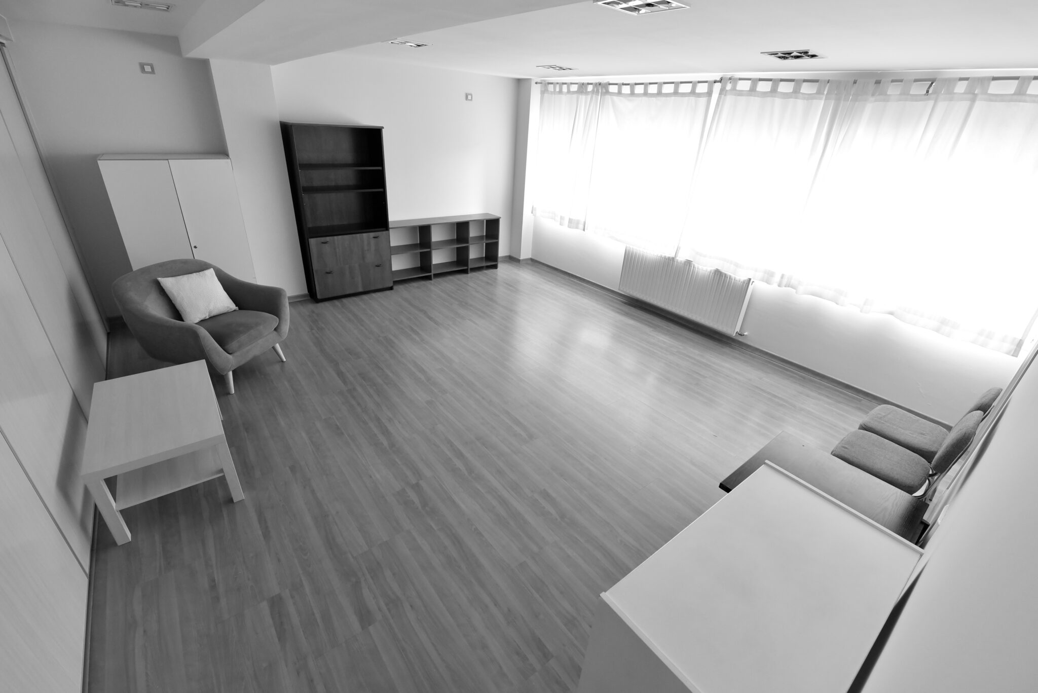 Despacho amplio de Lugo con sillones, mesa auxiliar, estantería baja y gran ventanal con cortinas.